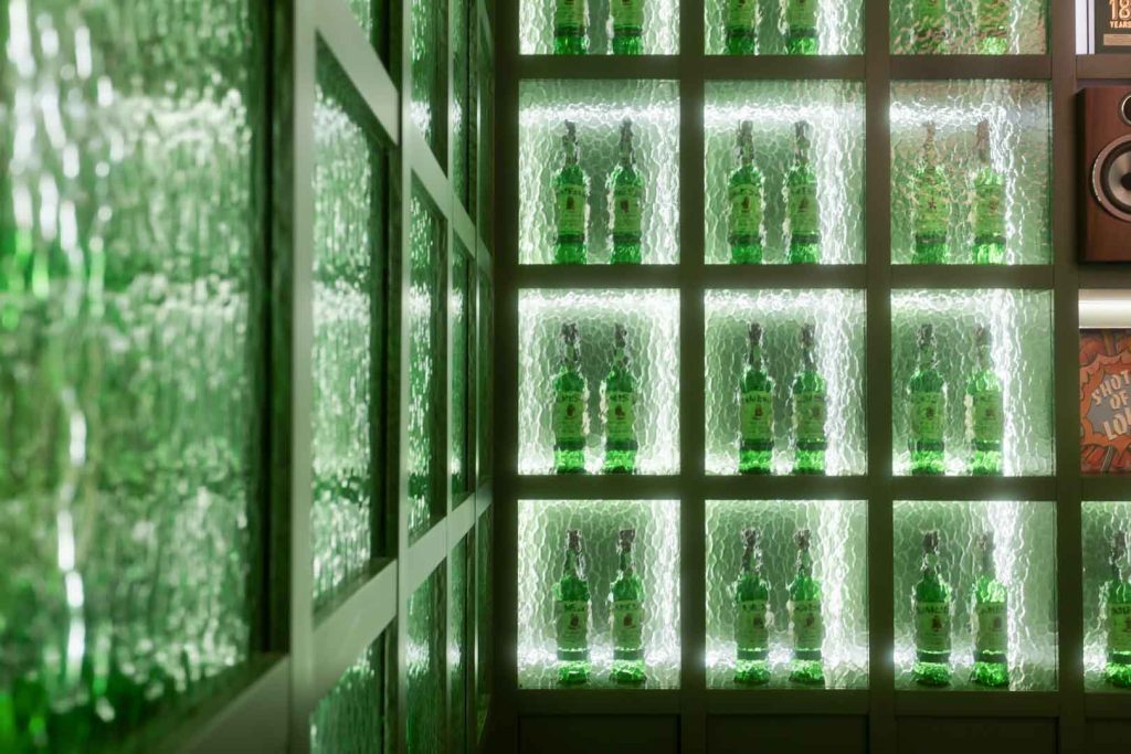Green glass bottles arranged on backlit shelves in a display fridge.
