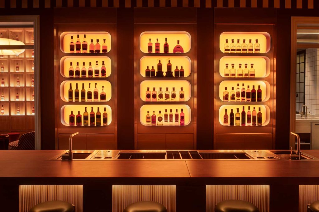Backlit shelves with liquor bottles arranged in rounded display niches behind a copper-toned bar.