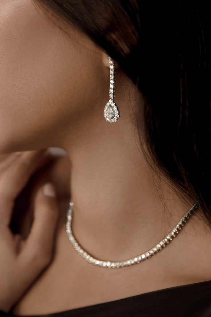 Close-up of a woman's neck wearing a diamond drop earring and a matching sparkling necklace.